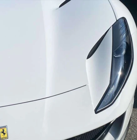 Close-up shot of a white luxury sports car highlighting the sleek headlight design and hood contour.