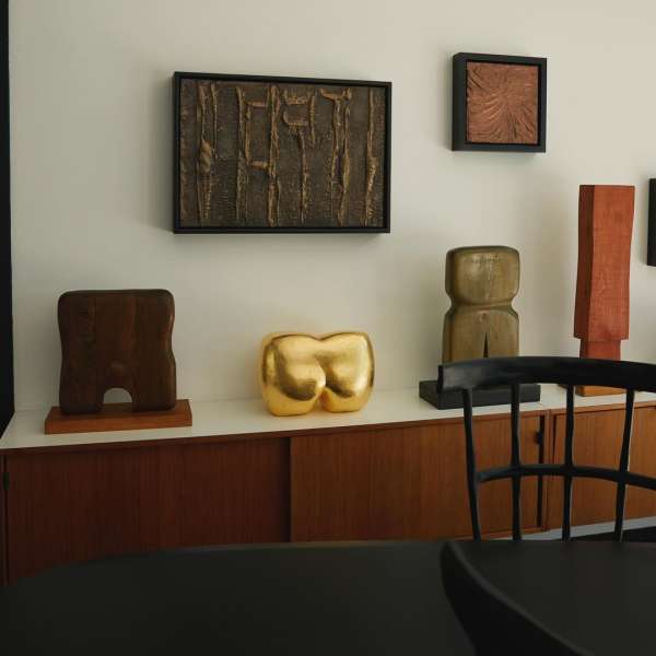 Interior view of multiple pieces of art on display, including sculptures and framed wall art, set against a neutral wall.