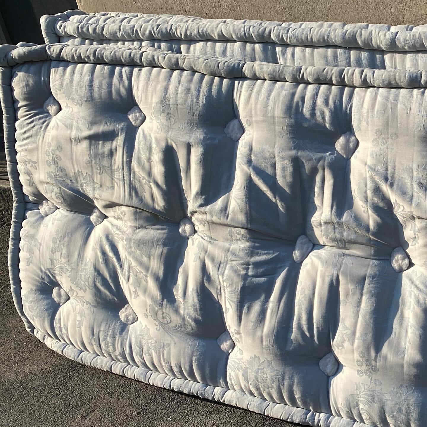 Close-up view of a large, patterned mattress with tufted buttons. The mattress appears aged and textured with visible wear and tear.