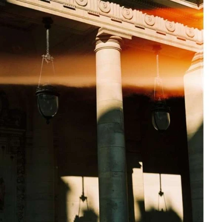 Architectural shot features concrete columns and hanging lamps casting shadows. The scene is bathed in warm, diffused natural light.