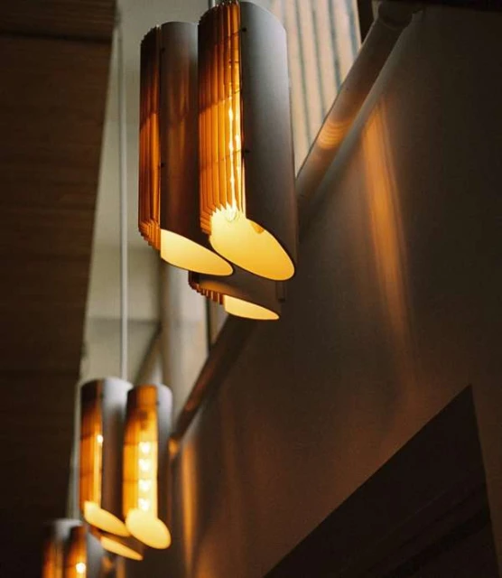 A line of cylindrical pendant lights cast a warm glow in a softly lit architectural interior with a neutral color palette.