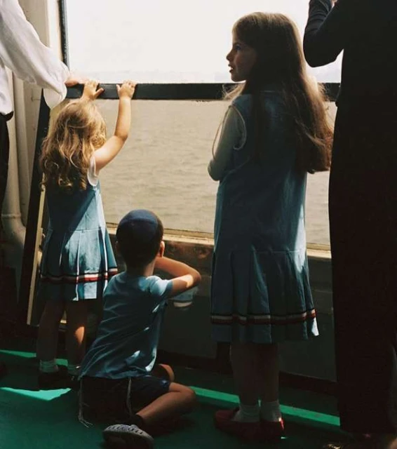 Three young children looking out over the water from the deck of a boat wearing matching blue outfits, enjoying a day out on the water.