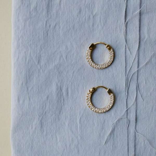 Close-up of pair of gold hoop earrings with diamonds on a light blue textured surface, suitable for jewelry advertising.