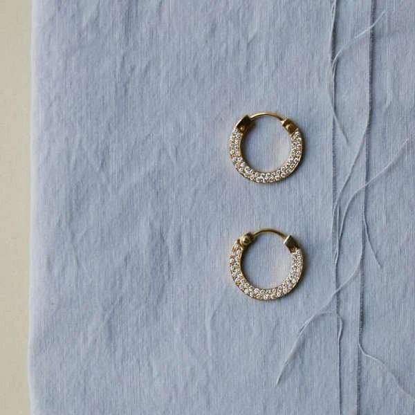 Close-up of pair of gold hoop earrings with diamonds on a light blue textured surface, suitable for jewelry advertising.
