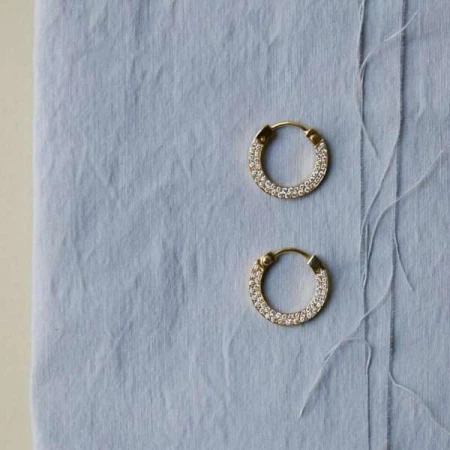Close-up of pair of gold hoop earrings with diamonds on a light blue textured surface, suitable for jewelry advertising.