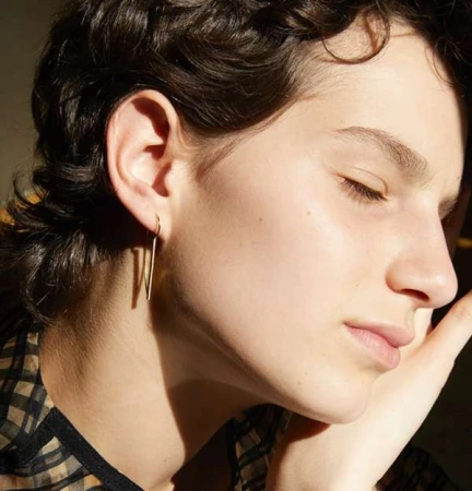Close-up profile of a woman with dark short hair wearing a slender gold drop earring and a plaid patterned top.
