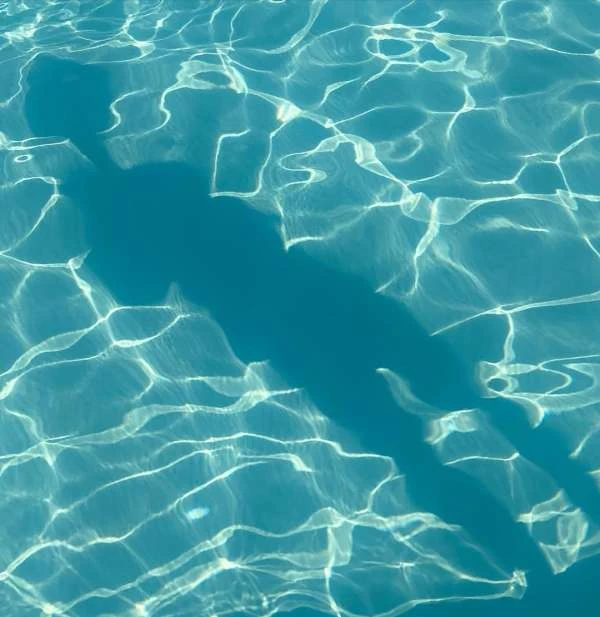 Underwater view of a shadow cast in a swimming pool, sunlight refracts and dances across the bottom creating light and dark patterns.