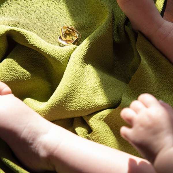 Close-up of a child's hands and feet resting on green textured fabric beside a gold ring, creating a soft, intimate image.