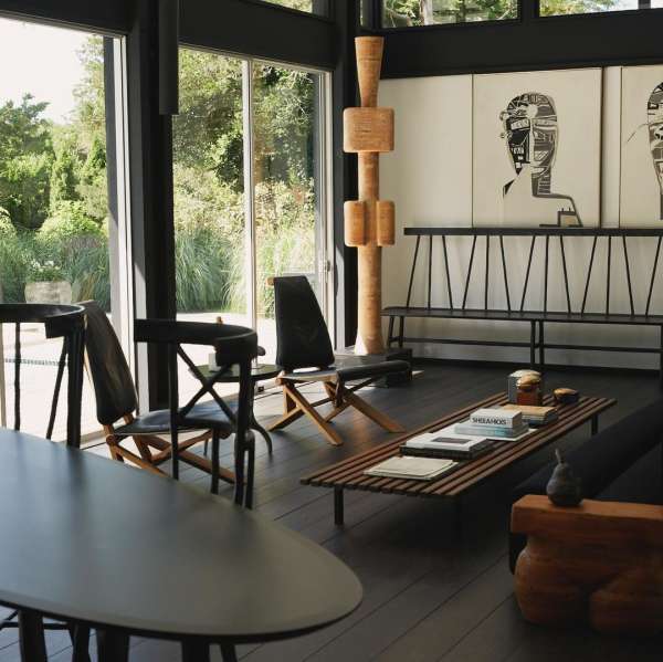Modern living room interior with black-framed windows, black wood floors, a wooden coffee table, and art on the walls, daytime.