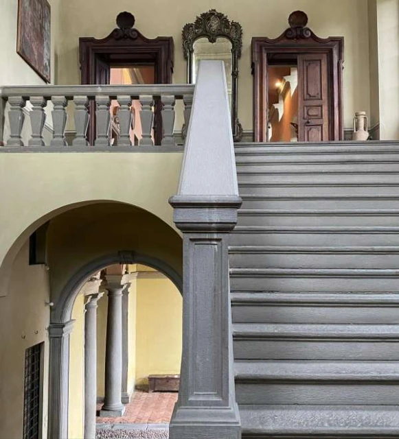 Ornate architectural interior featuring staircase with grey steps, a balustrade, and arches with columns in a building hallway.