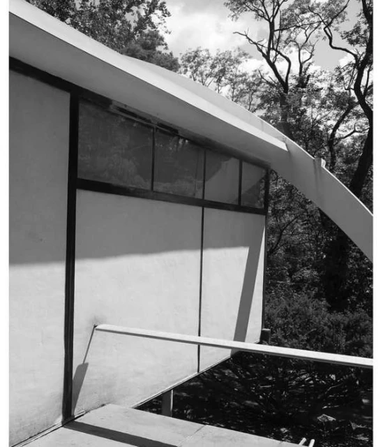 Black and white architectural image showcasing the exterior of a modern building with large windows and surrounding trees.