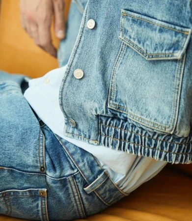 Close-up of a person wearing a denim jacket and jeans, showcasing light blue denim textures and silver button details in a casual setting.