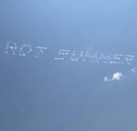 Skywriting in a blue sky that spells out 'HOT SUMMER' with puffy white clouds. The sky is a clear, vibrant blue, with only a few small clouds.