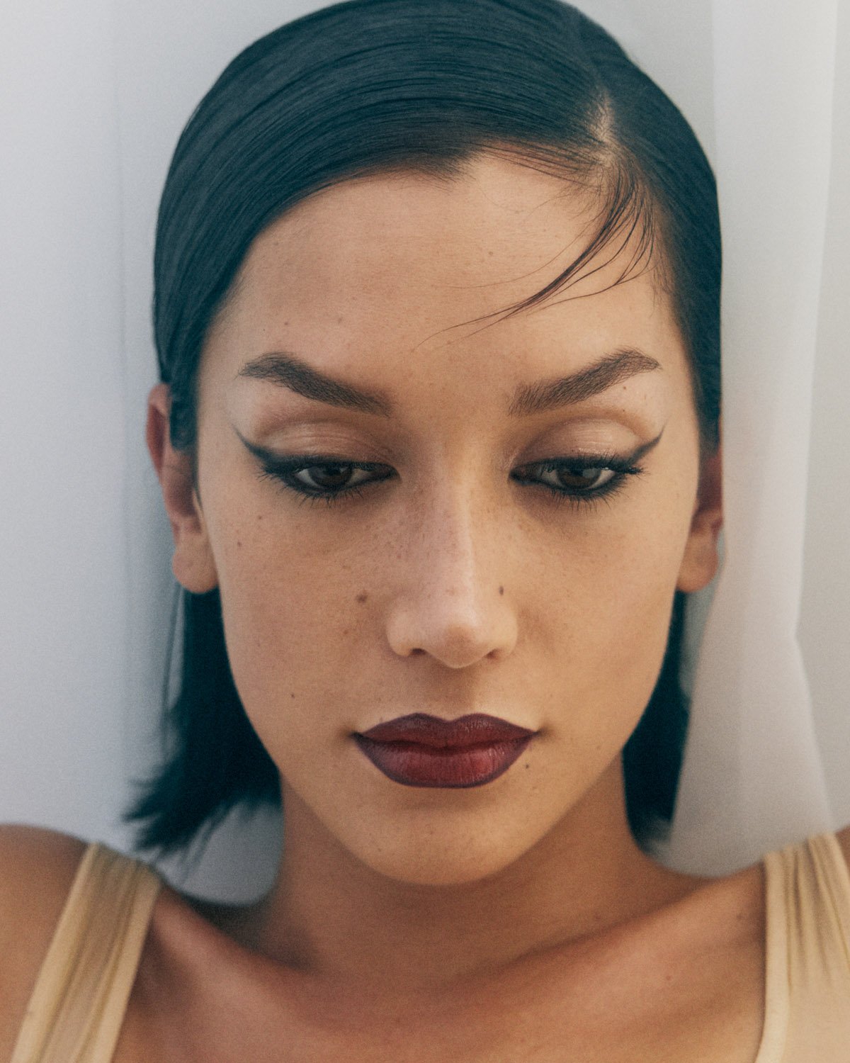 Close-up portrait of a woman with dark hair, wearing eyeliner and dark red lipstick, against a white background in a photo studio.