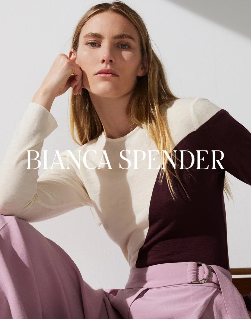 Blonde woman in a color-blocked top and pink trousers posing indoors for Bianca Spender fashion, lit by diffused natural light.