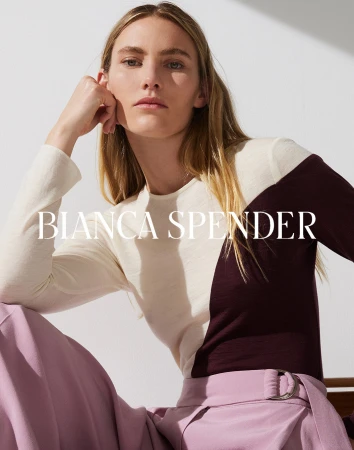 Blonde woman in a color-blocked top and pink trousers posing indoors for Bianca Spender fashion, lit by diffused natural light.