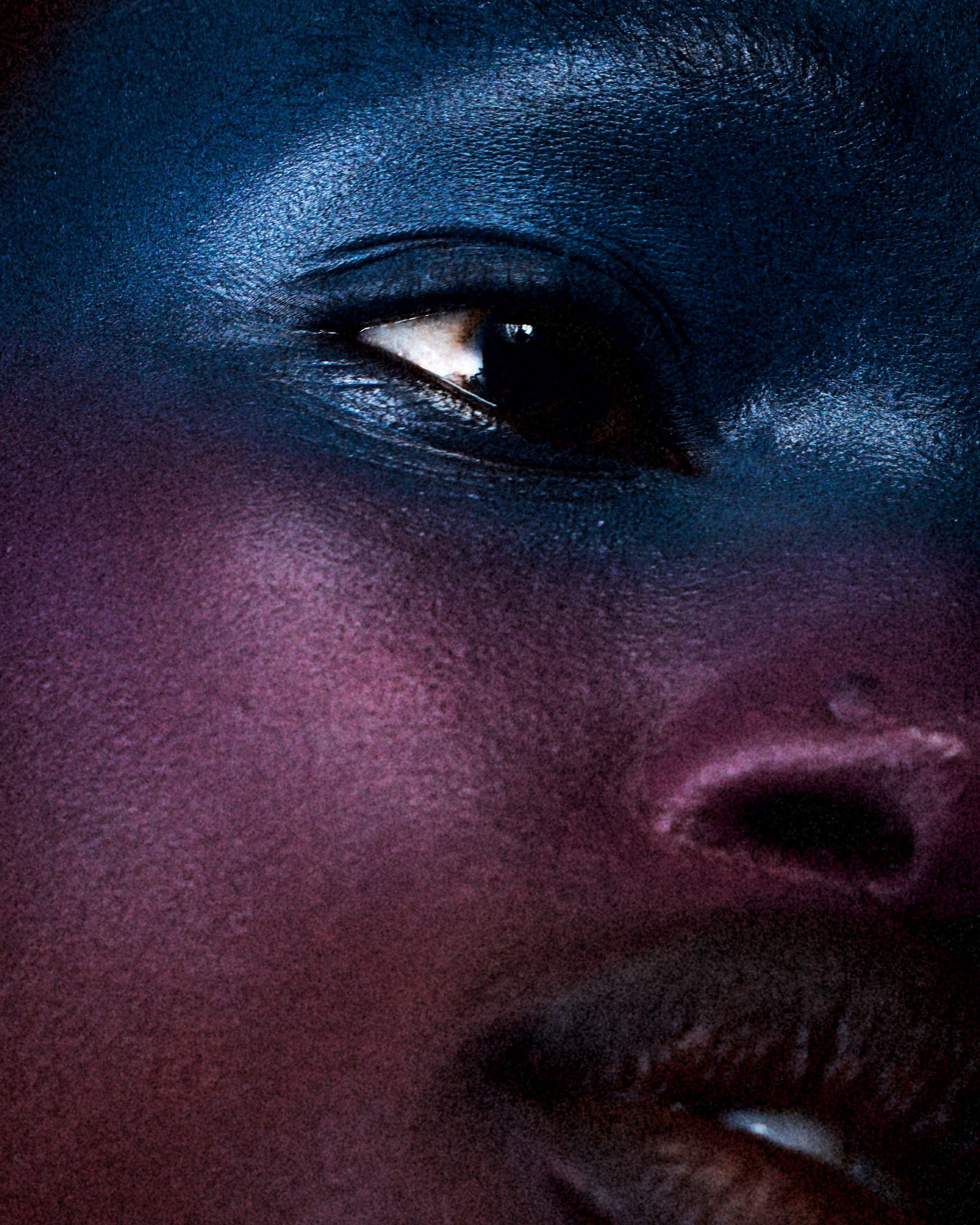 Close-up shot of a Black woman's face with dramatic blue and purple makeup creating a strong contrast and highlighting her features.