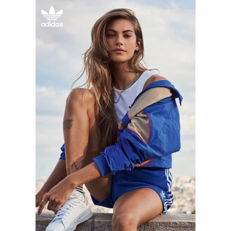Woman wearing blue athletic jacket and white top sitting on a rooftop against an open sky background.