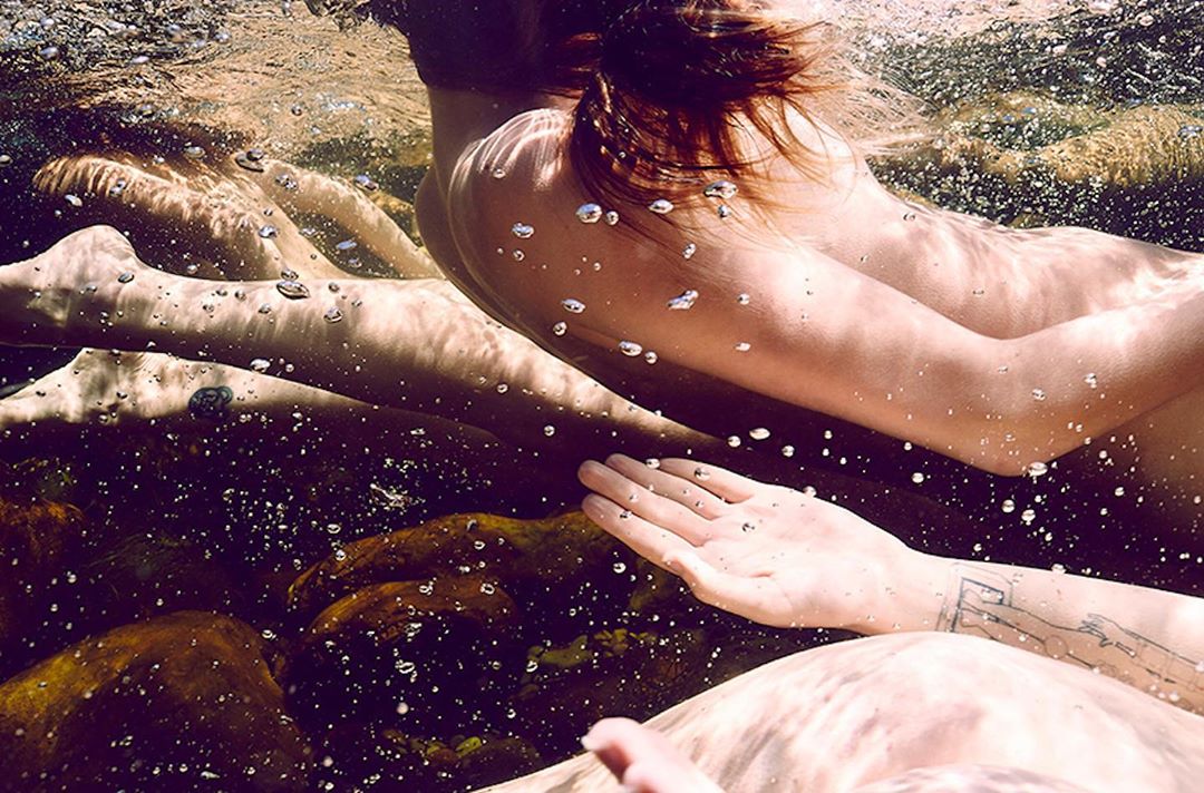 Underwater view of two people swimming, with light refracting through the water and illuminating the subjects in a natural setting.