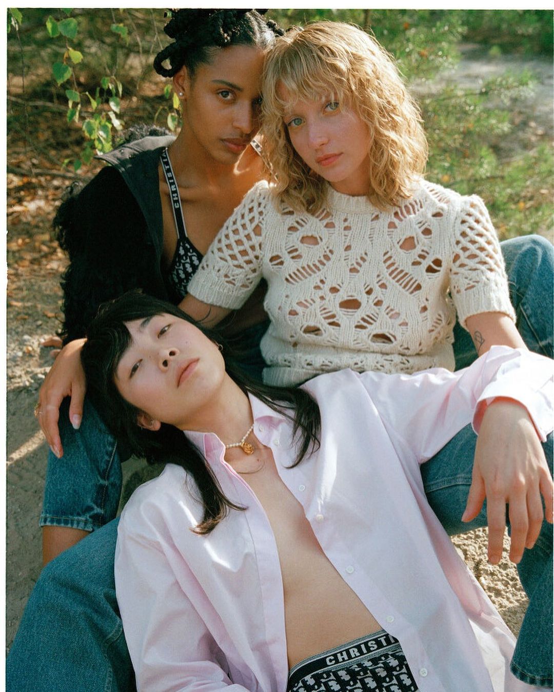 Three diverse women in outdoor fashion shot; one with blonde curly hair, one with dark hair up, one with pink shirt and black hair.