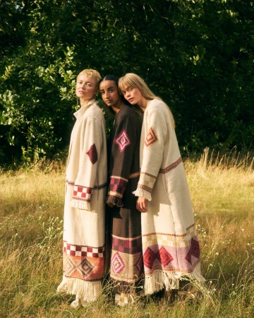 Three female models standing together in a grassy field wearing long patterned coats by photographer Caroline Mackintosh.