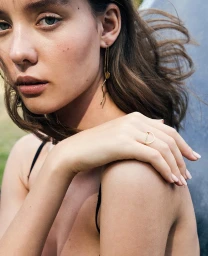 Close-up portrait of a woman wearing gold drop earrings and a thin gold ring, photographed in Paris by Caroline Mackintosh.