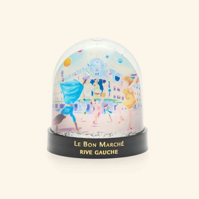 Snow globe featuring an illustration of people dancing in front of a building, with 'Le Bon Marché Rive Gauche' printed on the base.