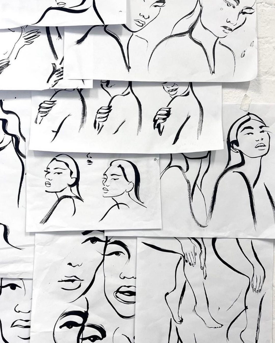 Wall display of black and white figure drawing sketches on paper; abstract line art of human faces and bodies; contemporary art.