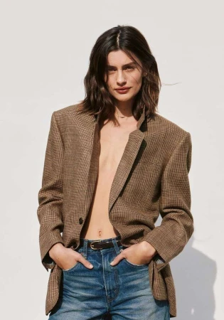 Woman wearing a brown houndstooth blazer and blue denim jeans against a plain white background