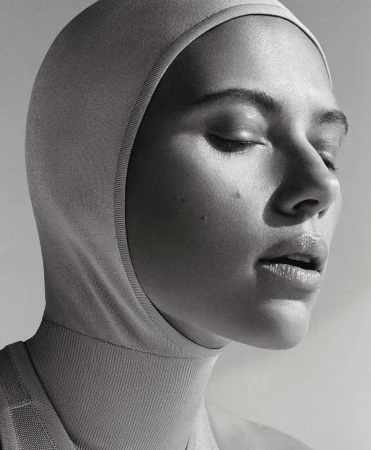 Monochrome portrait of a woman wearing a fitted hood covering her head and neck, with her eyes closed in soft lighting.