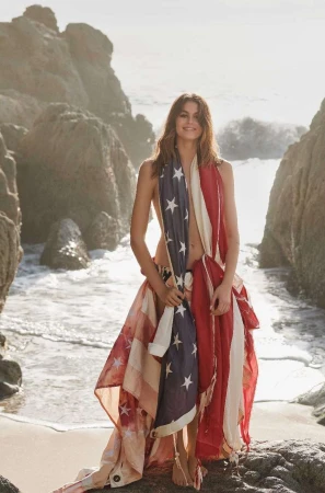 Model Kaia Gerber wearing an American flag wrapped as a garment on a rocky beach by Cass Bird