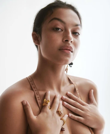 Portrait of an adult female with tanned skin and gold jewelry on her hands in a studio setting with a white background.