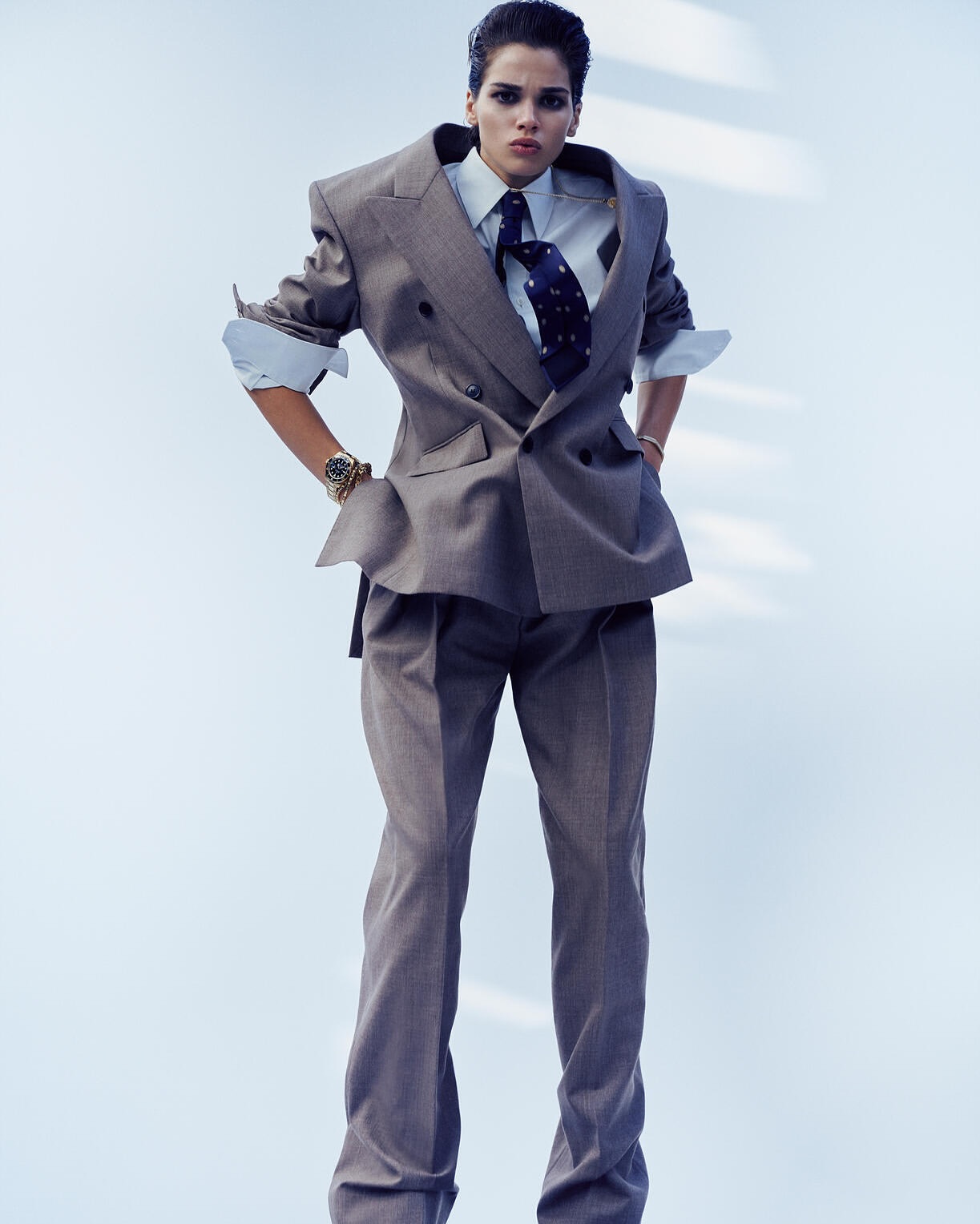 Model wearing an oversized grey double-breasted suit with white shirt and patterned tie against a light background