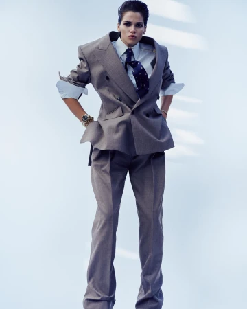 Model wearing an oversized grey double-breasted suit with white shirt and patterned tie against a light background