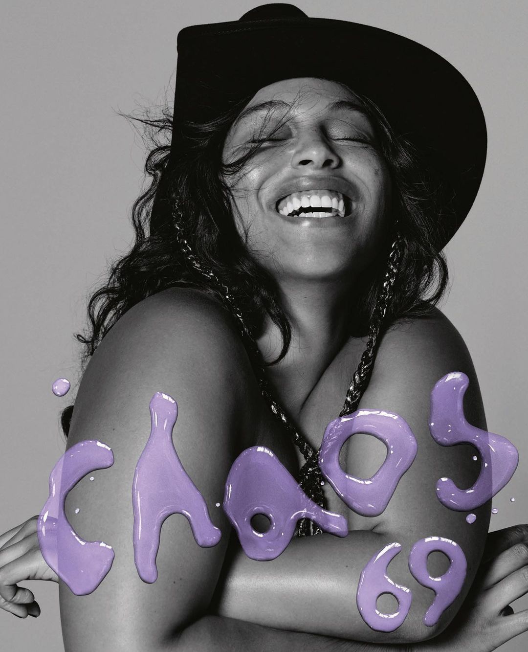 Close-up portrait of a laughing woman wearing a black hat with large purple lettering overlay reading CHAOS 69.