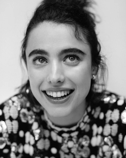 Black and white portrait of smiling woman with dark hair and patterned top against a plain background in eye-level close-up.