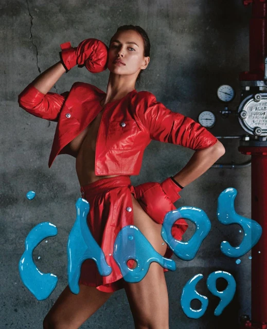 Fashion editorial shot of a woman in a red jacket, gloves, and skirt against a textured wall, emphasizing color and bold styling.