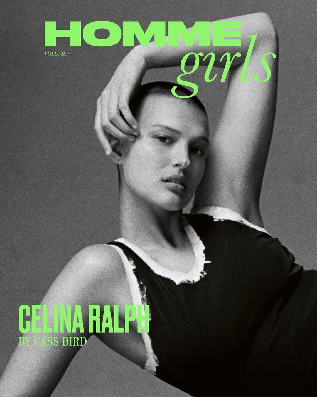 Black and white portrait of a bald woman wearing a dark tank top with white trim, posing with her arm raised behind her head.