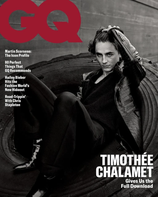 Timothée Chalamet on a GQ magazine cover posing on a tractor tire in a black jacket and pants with a moody, close-up shot.