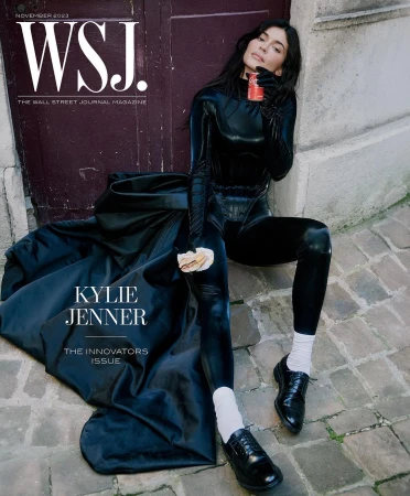 WSJ magazine cover featuring Kylie Jenner in a black bodysuit and black coat sitting on stone steps, holding a drink and pastry.