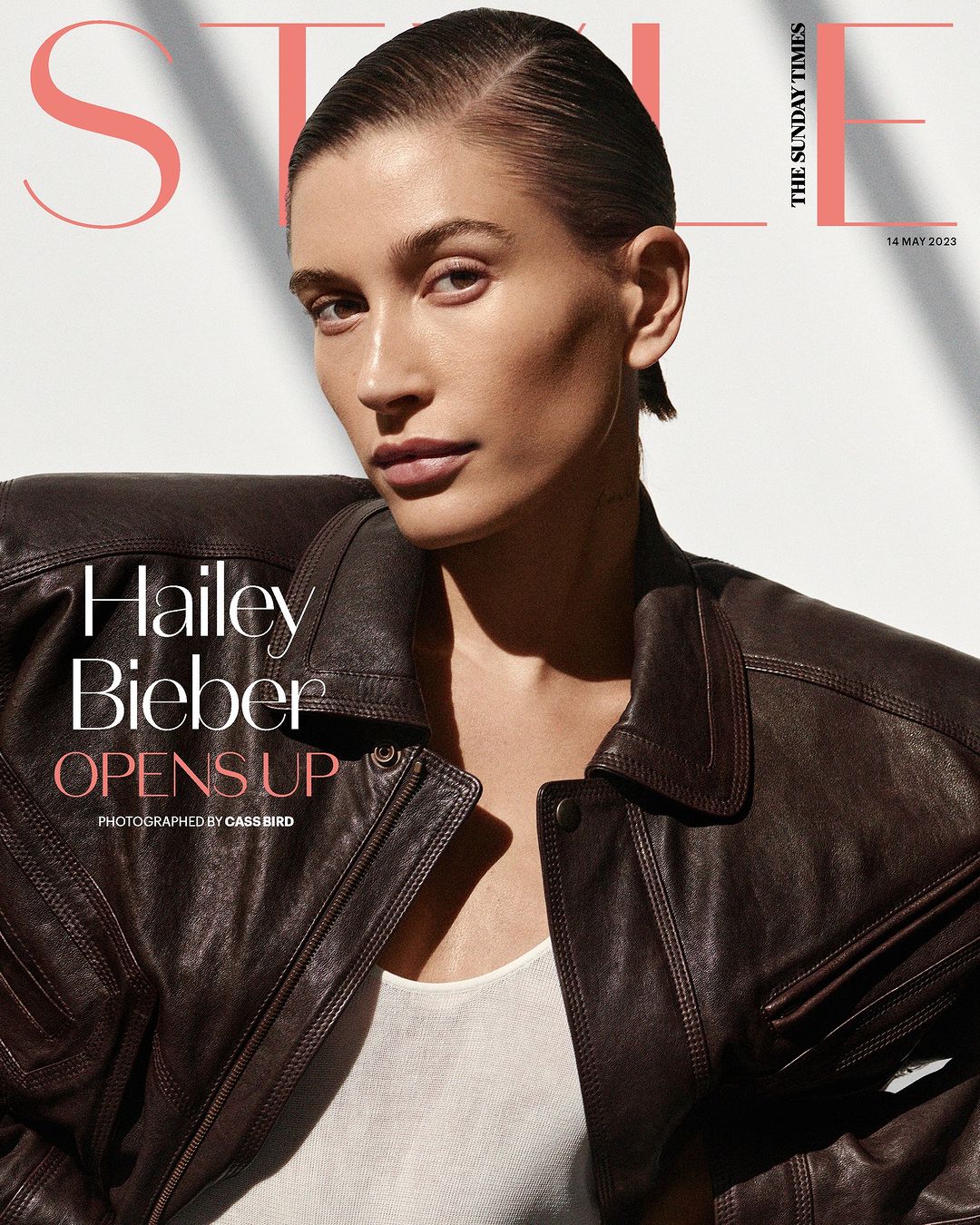 Hailey Bieber gazes forward on magazine cover. She wears a brown leather jacket and light shirt against a blurred backdrop.