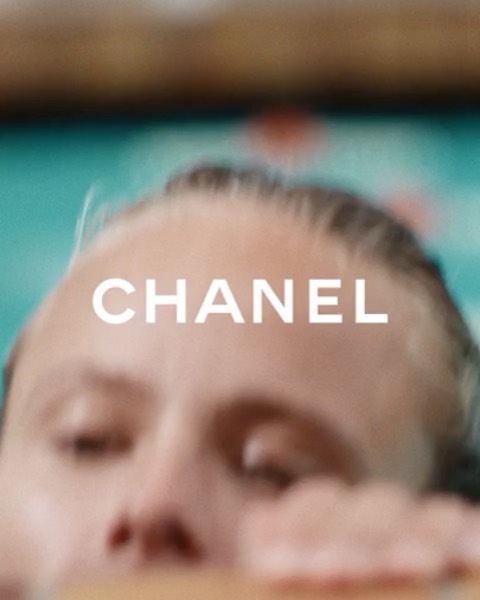 Close-up of a person's face partially submerged in water with 'CHANEL' text overlayed. Focus on skin texture, light refraction and clean aesthetic.
