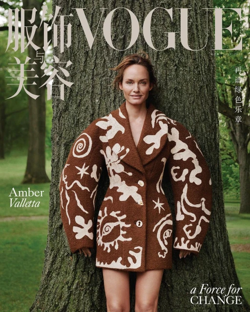Amber Valletta on Vogue cover: woman poses in patterned coat next to large tree trunk outdoors with soft focus green background.