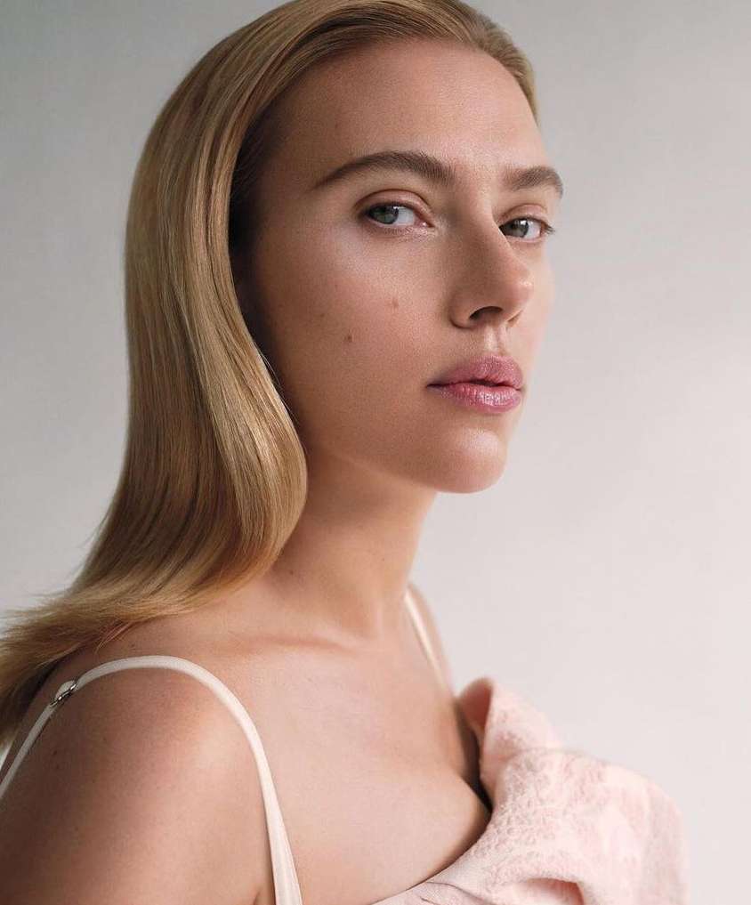 Portrait of a woman with blonde hair, wearing a light-colored top, in a studio setting with a soft, neutral background.