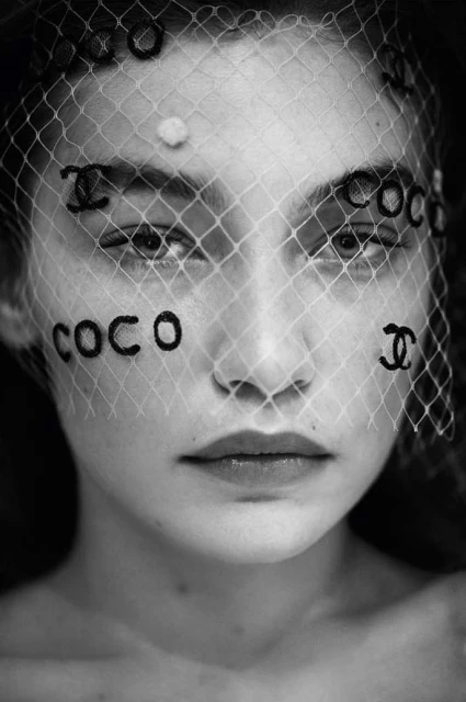 Black and white portrait of a woman with netting veil, featuring brand logos and text, showcasing beauty and fashion elements.