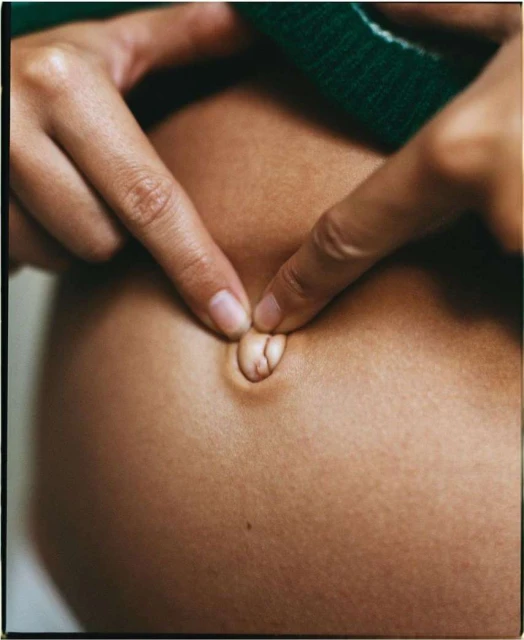 Close-up shot of a pregnant woman's belly with fingers touching her navel, highlighting the beauty and anticipation of motherhood.