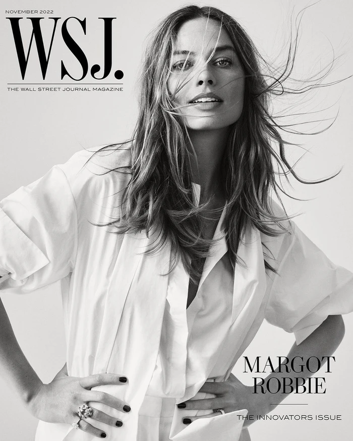 Black and white portrait of Margot Robbie with wind-blown hair wearing a white shirt against a seamless background