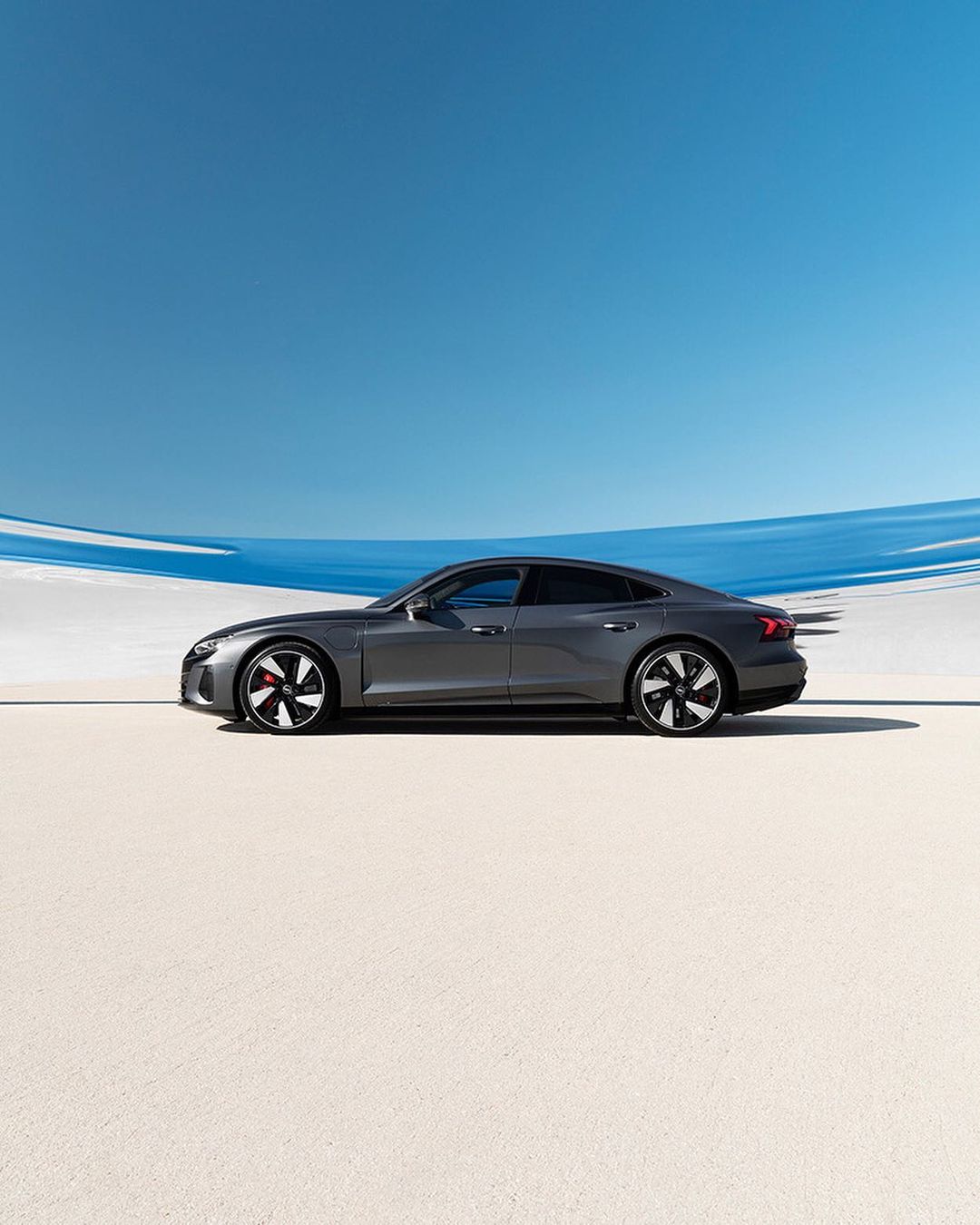 Sleek grey Audi e-tron GT electric car showcased in a minimalist setting with a clear blue sky in a product photography style, automotive excellence.