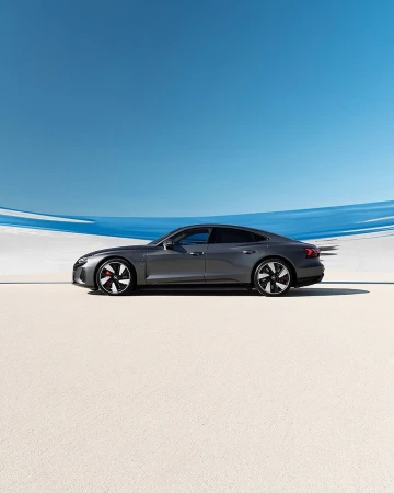 Sleek grey Audi e-tron GT electric car showcased in a minimalist setting with a clear blue sky in a product photography style, automotive excellence.