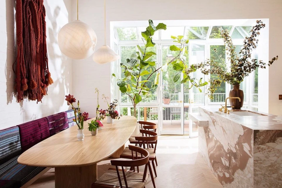 Bright and airy dining room features a long wooden table, wooden chairs, and bench seating, accented by fresh flowers and greenery.